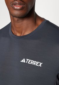 Dark gray Terrex t-shirt with a crew neckline features a white logo on the left chest area. Smooth fabric texture, short sleeves.