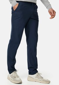 Navy blue, stretchy pants with a slim fit, featuring side pockets and detailed seams. Paired with light-colored, textured sneakers.