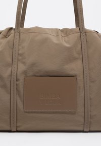 Bolso tote de nailon khaki con detalles de costura, asas dobles y un parche rectangular de cuero con la inscripción "BIMBA Y LOLA" en relieve. Textura suave.