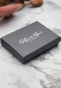 Grå texturerad smyckesask med en slät yta, som har en silverfärgad logotyp på toppen. Rektangulär form med ett platt lock.