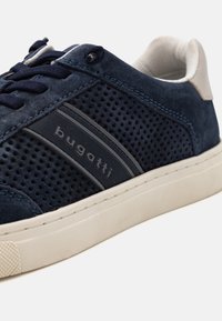 Kék velúr sportcipő perforált oldalakkal, gumitalppal és "bugatti" logóval a sötét színű kiemelő csíkon. Krém színű belső és varrási részletek.