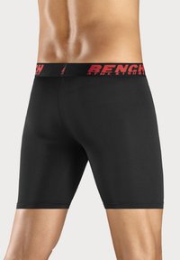 Black athletic shorts with a tight fit, featuring a red elastic waistband displaying the "BENCH" logo. Smooth texture and mid-thigh length.
