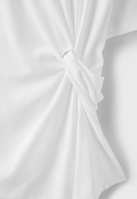 Tissu blanc torsadé en nœud, montrant la texture et les plis sur un fond blanc uni.
