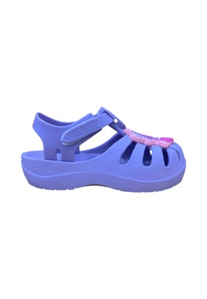 Sandalia infantil morada con puntera cerrada, tira ajustable, orificios de ventilación y elementos decorativos rosas en la parte superior.