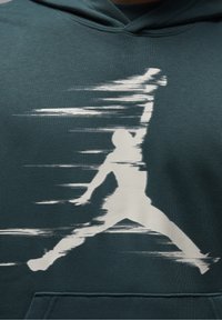 Sudadera color azul verdoso con un gráfico blanco de una figura saltando con líneas de movimiento, hecha de una tela suave, que muestra un bolsillo tipo canguro en la parte frontal.