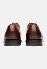 Braune Lederschuhe mit einem eleganten Design, abgerundeten Fersen, kontrastierenden Nähten und einer glatten Oberfläche. Holzabsätze für zusätzliche Stabilität.