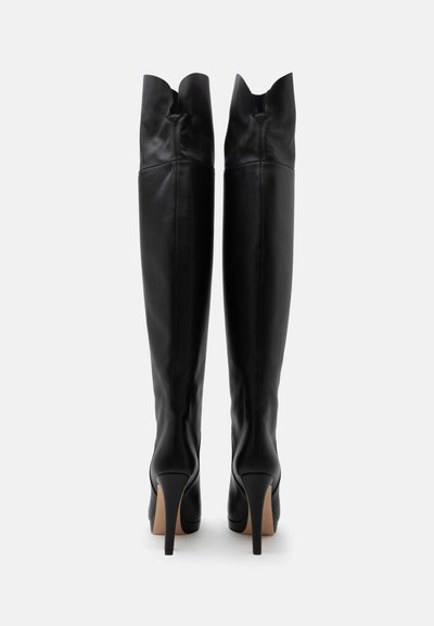 Paire de bottes hautes en cuir noir avec talons pointus, vues de dos sur fond blanc uni.