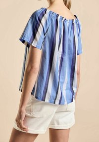 Haut à rayures bleu en tissu léger avec un design décolleté aux épaules, présentant des rayures violettes, blanches et noires.