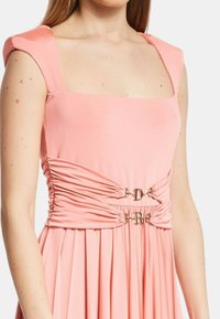 Abito aderente rosa con scollo quadrato, gonna plissettata e ruches in vita. Presenta accenti in metallo dorato con le iniziali "D" e "R".