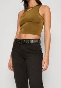 Top corto verde oliva con un corte en forma de llave en el escote, combinado con pantalones vaqueros negros de tiro alto y un cinturón negro con ojales.