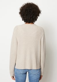 Maglione beige lavorato a maglia con un fit rilassato, caratterizzato da una lavorazione a coste sulla parte delle spalle e sulla schiena, maniche lunghe e orlo arrotondato.