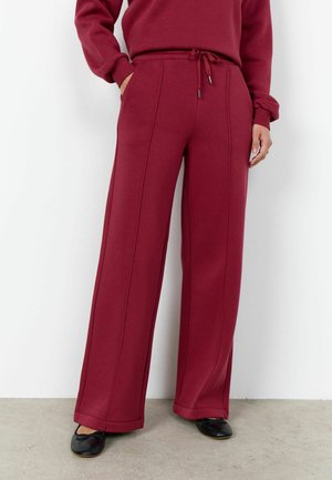 Osoba ubrana w bordowe spodnie z wysokim stanem i szerokimi nogawkami, z wiązaniem w pasie, w połączeniu z bordową bluzą i czarnymi balerinami.