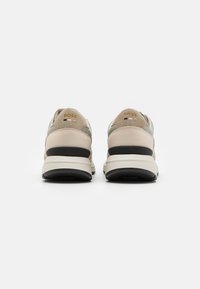 Beige und graue Sneaker mit strukturiertem Wildleder-Obermaterial, schwarzer Gummisohle und goldfarbenen Logodetails an der Ferse. Klassische und moderne Designelemente.