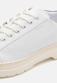 Hvite lær sneakers med teksturert overdel, runde snøringshull og HUGO-merke. Har en kremfarget gummisåle med mønstrete såle.