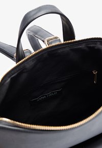 Black leather backpack with gold zipper and smooth texture. Interior features black lining and a zipped pocket labeled "ANNA FIELD."
