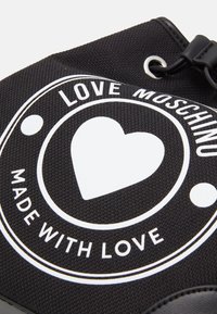 Svart textilväska med en vit grafik som har ett hjärta, texten "LOVE MOSCHINO" och "MADE WITH LOVE", samt släta läderaccenter.