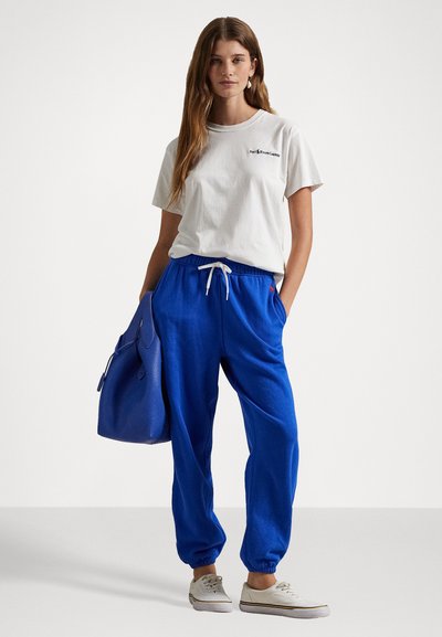 Balta medvilninė marškinėliai su logotipu, mėlynos sportinės kelnės su elastingais raišteliais bei juosmeniu, ir mėlynas tekstūruotas delninukas. Atsitiktiniai sportbačiai puikiai užbaigia aprangą.