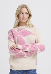 Pull en laine beige avec motif floral rose et blanc, encolure ronde et manches longues. Texture douce avec coupe décontractée.