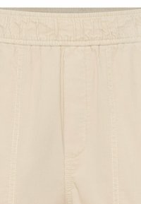 Pantalons beiges avec taille élastique, texture à côtes verticales, coutures avant et poches latérales. Tissu léger adapté à un usage décontracté.