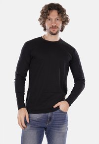 T-shirt nero a maniche lunghe con scollatura a girocollo, realizzato in morbido cotone. La vestibilità è casual, abbinata a jeans in denim blu.
