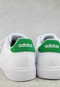 Baskets blanches en cuir lisse, avec des cols rembourrés et des accents verts au niveau du talon. Présente le logo "adidas" en blanc sur le patch vert.