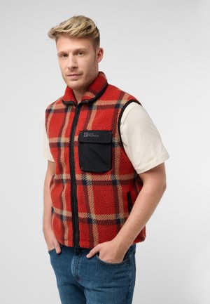 Rode en geruite fleece vest met een zwarte rits, voorzien van een voorklep en een hoge kraag. Gedragen over een crèmekleurig shirt met korte mouwen.