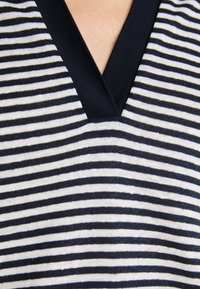 V-hals stripet genser med en marineblå og kremfarge-fargepalett. Har horisontale striper og ribbestrikket tekstur ved halslinjen.