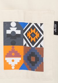 Sac en coton avec un design imprimé coloré présentant des motifs géométriques en orange, bleu, noir, gris et blanc sur un fond crème.