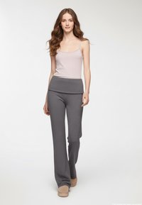 Jasnoszary top na ramiączkach w połączeniu z ciemnoszarymi, wzorzystymi spodniami o szerokiej nogawce oraz beżowymi butami wsuwanymi, podkreślającymi miękkie tekstury i luźny krój.