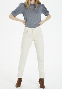Jeans de tiro alto en beige claro con corte recto, combinados con una blusa de manga corta de textura azul con un escote con volantes.