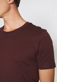 Bordeauxkortärmad T-shirt med rund hals och textilstruktur. Har en figurnära silhuett och minimal sömnadsdetalj.