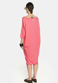 Oversized różowa sukienka o luźnym kroju, z szerokim dekoltem i rękawami o średniej długości. Miękka tkanina i subtelny detal z logo z tyłu.