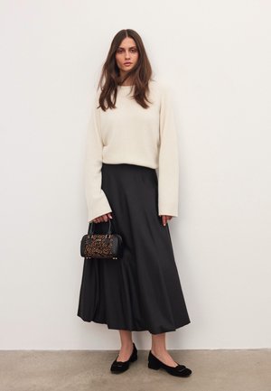 Suéter de punto crema, falda de satén negra, bailarinas negras con detalle de lazo y un pequeño bolso negro con acentos de estampado de leopardo.