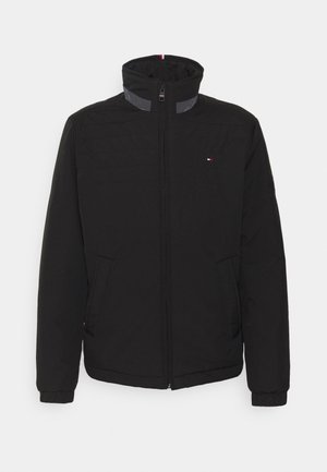 Veste noire à fermeture éclair avec col montant et deux poches avant, avec un petit logo rouge, blanc et bleu sur la poitrine gauche.