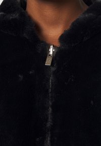 Zwarte nepbont zip-up jack met een capuchon, met een glanzende zilveren rits. Zachte textuur, geen zichtbare patronen en een close-up van het halsgebied.