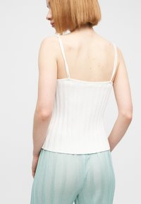 Λευκό κοντό μπλουζάκι με λεπτές τιράντες, εφαρμοστή γραμμή και λεία υφή. Συνδυασμένο με ανοιχτό πράσινο παντελόνι με κάθετες ρίγες.