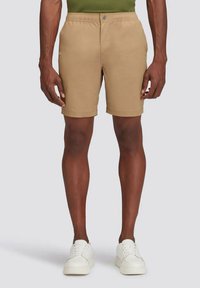 Pantaloni corti khaki con vita elastica, chiusura a bottone e orlo che arriva sopra il ginocchio. Indossati con sneakers bianche. Tessuto liscio.