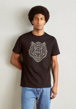 Camiseta de algodón negra con un gráfico de oso beige, mangas cortas y cuello redondo, combinada con jeans de mezclilla azul claro.