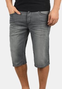 Bermudas de mezclilla gris con un corte relajado, diseño hasta la rodilla, cinco bolsillos y sutiles detalles de desgaste y decoloración.