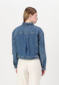 Keskmise pesu denim-jakk, millel on krae, seljapealne voldik ja nööbilised aksendid varrukatel. Omab lühendatud lõiget ja nähtavat õmblust.