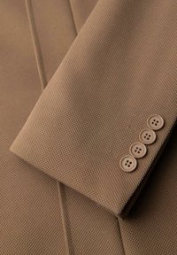 Braun strukturiertes Gewebe mit maßgeschneidertem Design, ausgestattet mit vier cremefarbenen Knöpfen an den Manschetten, die die klaren Linien und gleichmäßige Webart hervorheben.