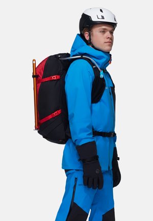 Blau wasserdichte Jacke und Hose mit schwarzen Akzenten, ausgestattet mit einem schwarzen Rucksack mit roten Gurten und einem Trinkschlauch. Weißer Helm.