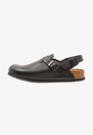 Schwarze synthetische Clogs mit geschlossenem Zeh, verstellbarem Riemen und Korkakzenten an der Ferse. Strukturiierte, rutschfeste Sohle für Halt.