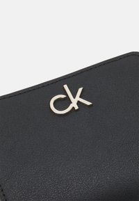 Black leather wallet featuring a gold "ck" logo on the front, with a smooth texture and clean, minimal design.