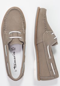 Chaussures en cuir brun clair avec des coutures blanches, design à lacets et semelle blanche contrastante, présentant des découpes sur les côtés pour la ventilation.