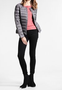 Grå dunjakke med vandret quiltet design, kombineret med en pink top og sorte slim fit jeans, suppleret med sorte ankelstøvler.