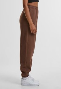 Bruine katoenen joggers met een elastische tailleband en zijzakken, met een taps toelopend ontwerp. Gecombineerd met witte sneakers.