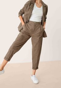 Olijfgroene, geperforeerde stoffen broek met een relaxte pasvorm, hoge taille, opgerolde zomen en steekzakken, gecombineerd met een witte tanktop en sneakers.