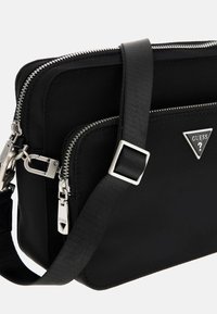 Black fabric shoulder bag with dual zip compartments, silver hardware, adjustable strap, and logo triangle accent on the front.