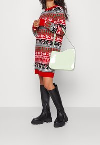 Robe-pull tricotée avec motifs rouges, verts et noirs ; sac à main vert menthe brillant ; bottes noires montantes à semelles épaisses.